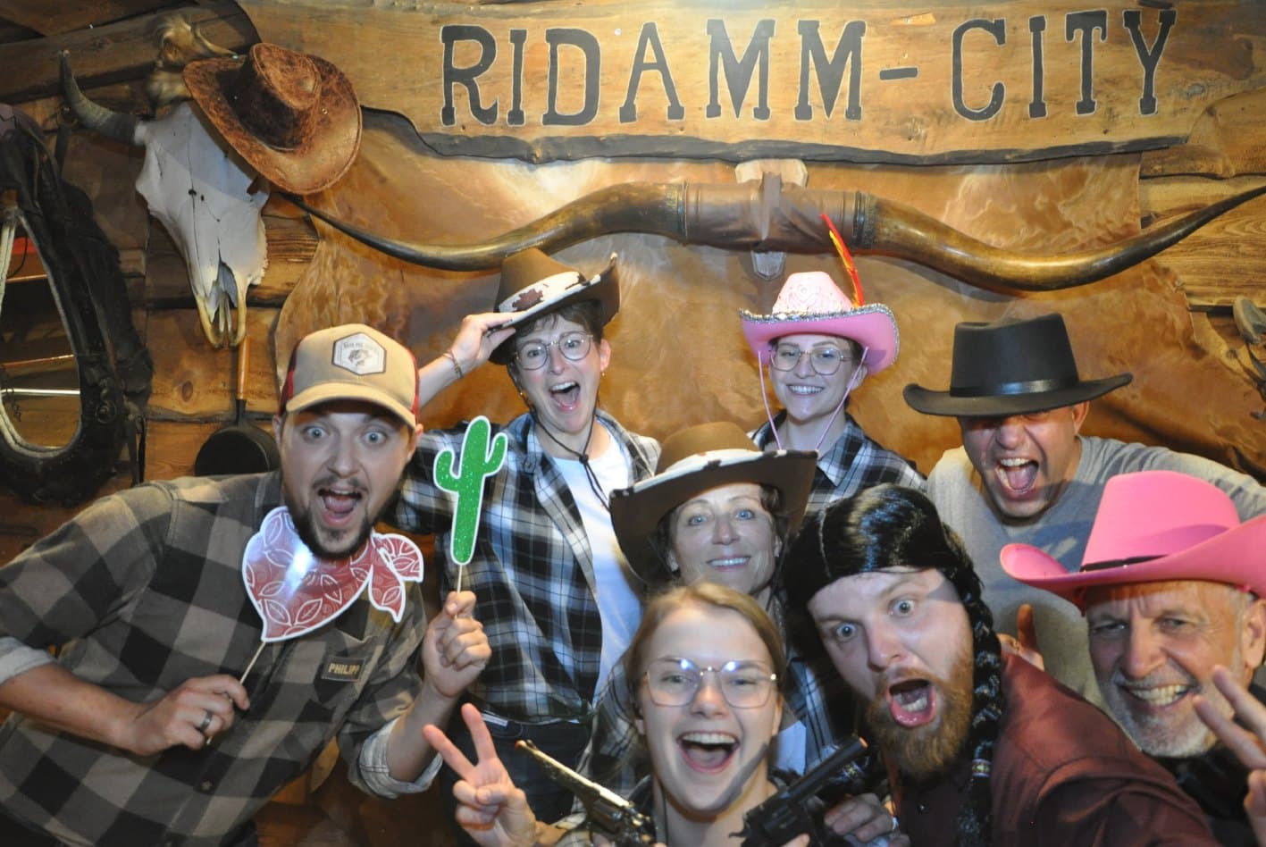 Gäste mit Cowboyhüten, Spielzeugrevolvern und Requisiten vor der Holzwand mit dem Ridamm-City-Schriftzug