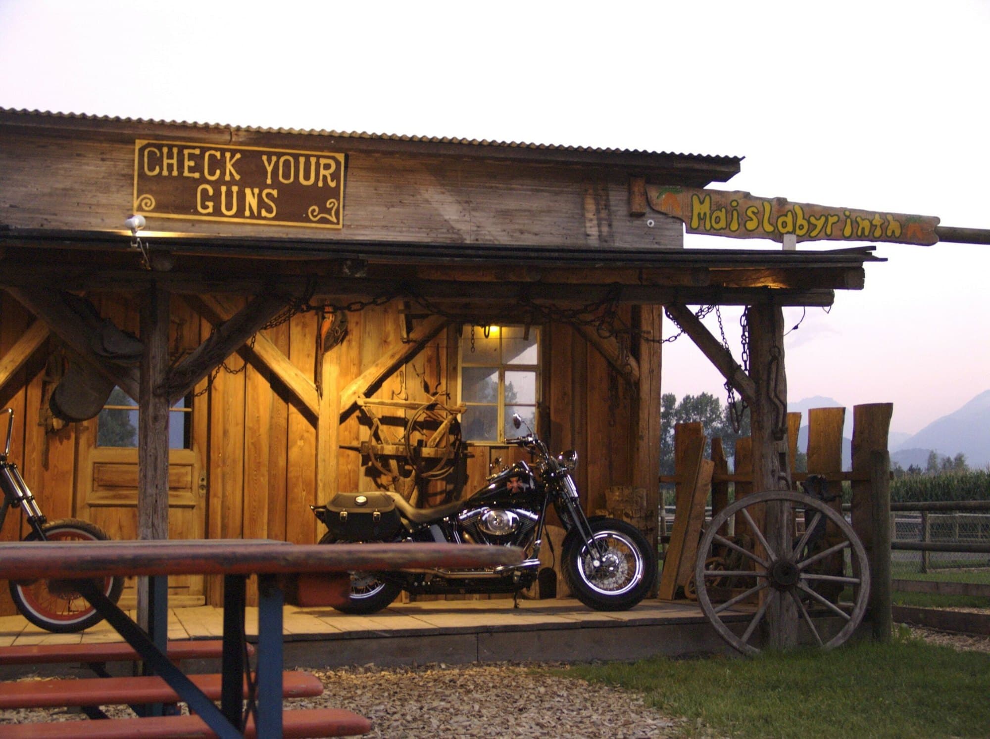 Der Saloon «Check your guns» in der Abenddämmerung mit einem Motorrad davor
