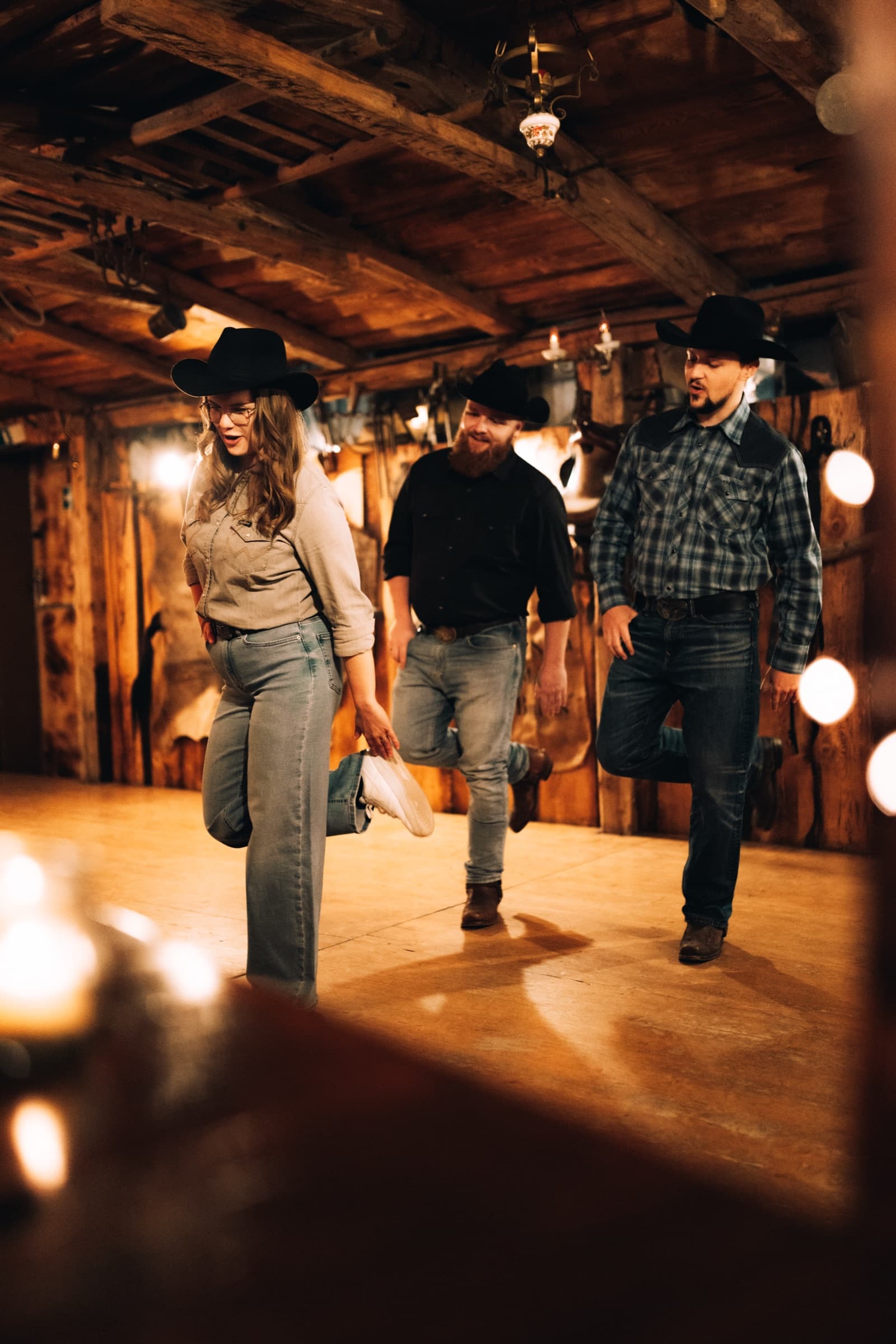 Drei Personen mit Cowboyhüten tanzen Line Dance im Saloon